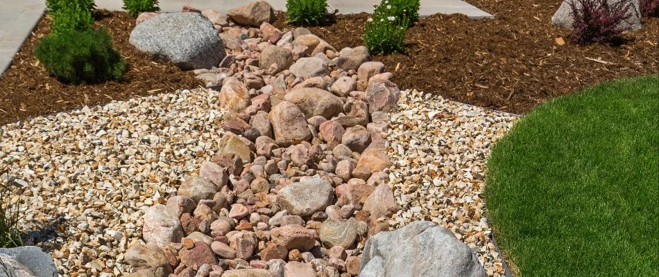 Landscaped dry creek bed with rocks and surrounding mulch and grass.